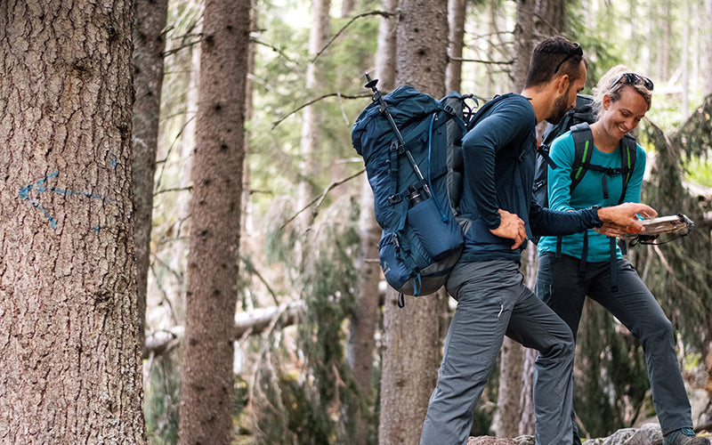 A man and woman hiking in the woods with backpacks on looking at their map