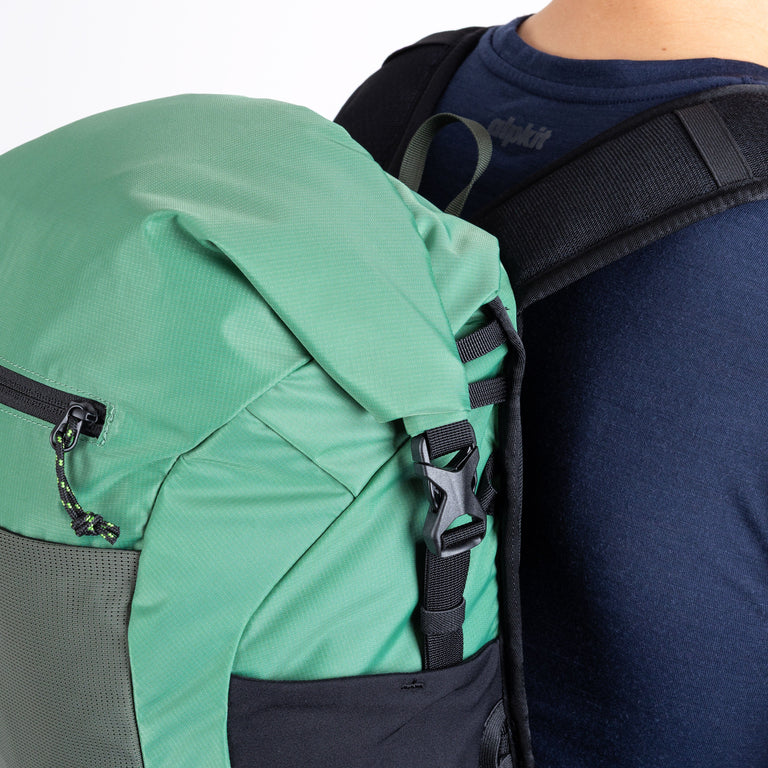 Green and gray backpack on a person's back with a focus on the straps and zippers.