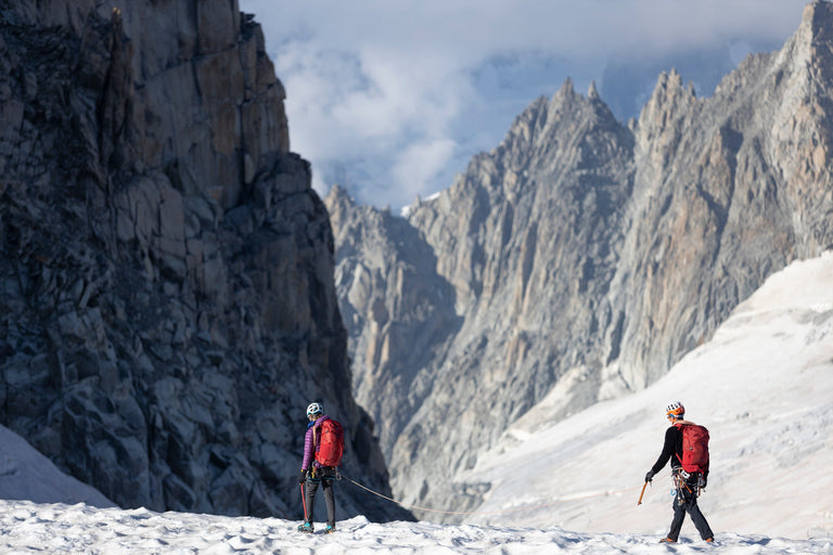 A woman walking across snow covered mountains in a purple down jacket - closed